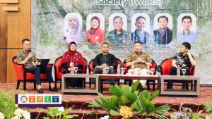 Moderator berbicara menggunakan mikrofon sementara empat narasumber duduk di panggung Simposium Internasional IWoRS XVIII.