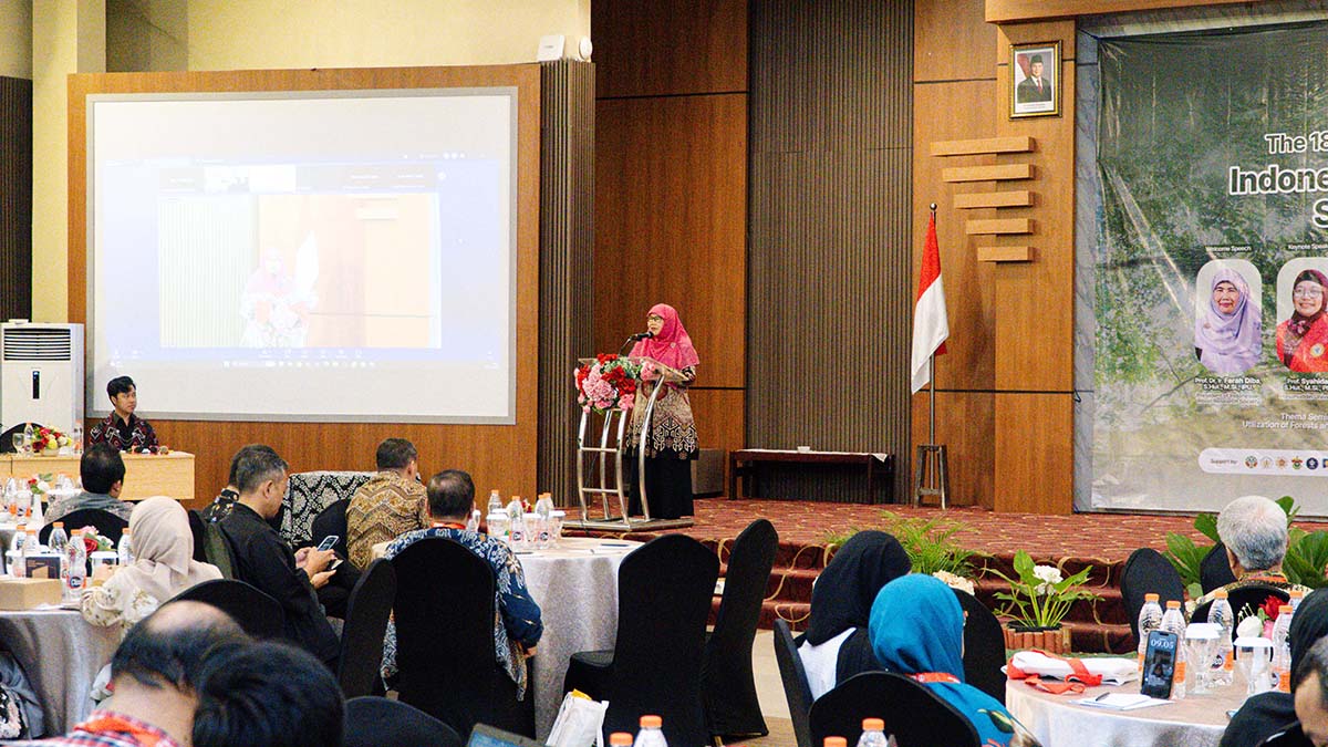 Prof. Farah Diba menyampaikan sambutan dari podium, dengan layar siaran dan peserta IWoRS XVIII di ruangan.