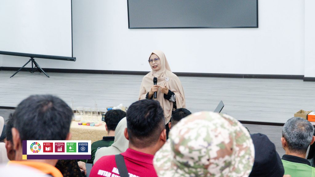 Prof. Emi Roslinda memegang mikrofon saat menyampaikan materi di hadapan peserta, dengan ikon SDGs di sudut kiri bawah foto.