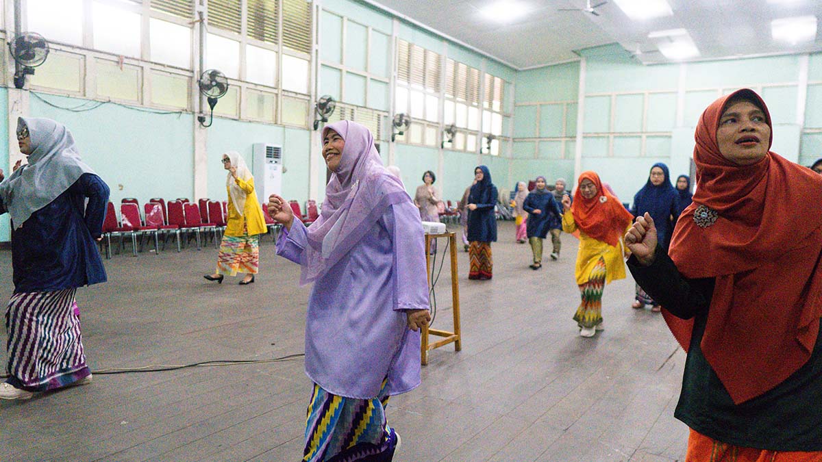 Prof. Farah Diba berbaju kurung ungu menari jepin bersama peserta lain di dalam aula.